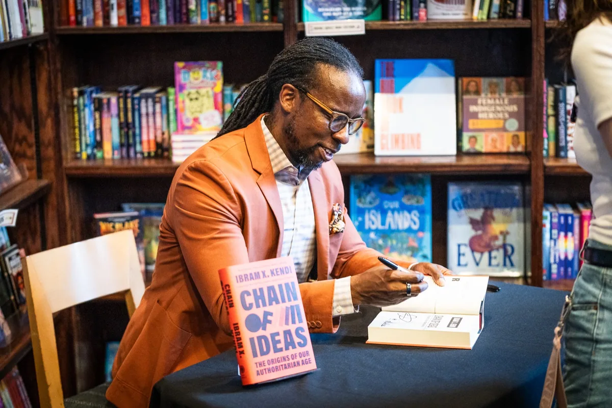 An author signing a book in front of bookstore shelves