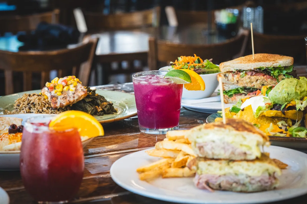 Sandwiches, an entree, nachos, and colorful drinks on a restaurant table