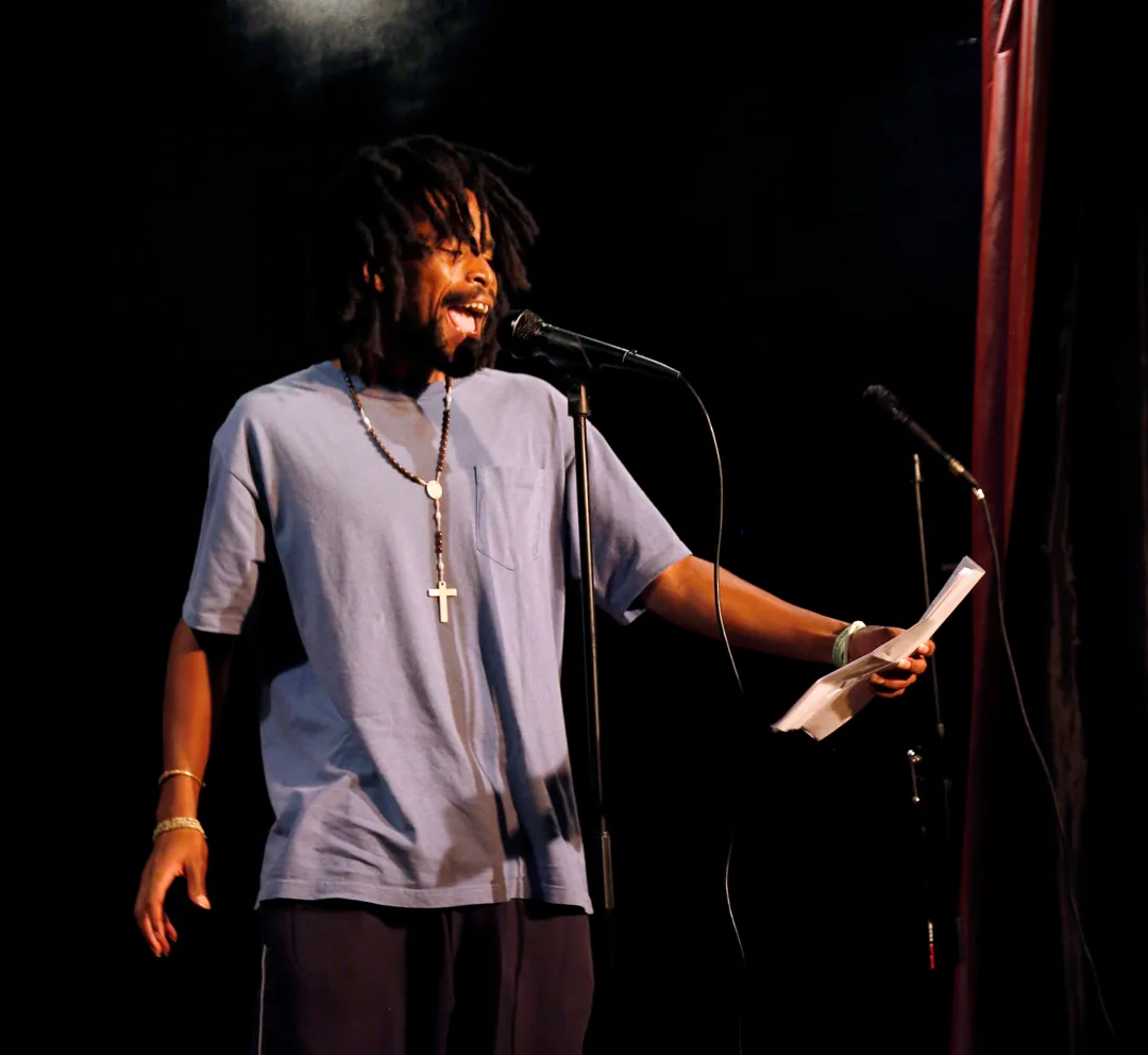 A poet performing at a microphone while holding a page